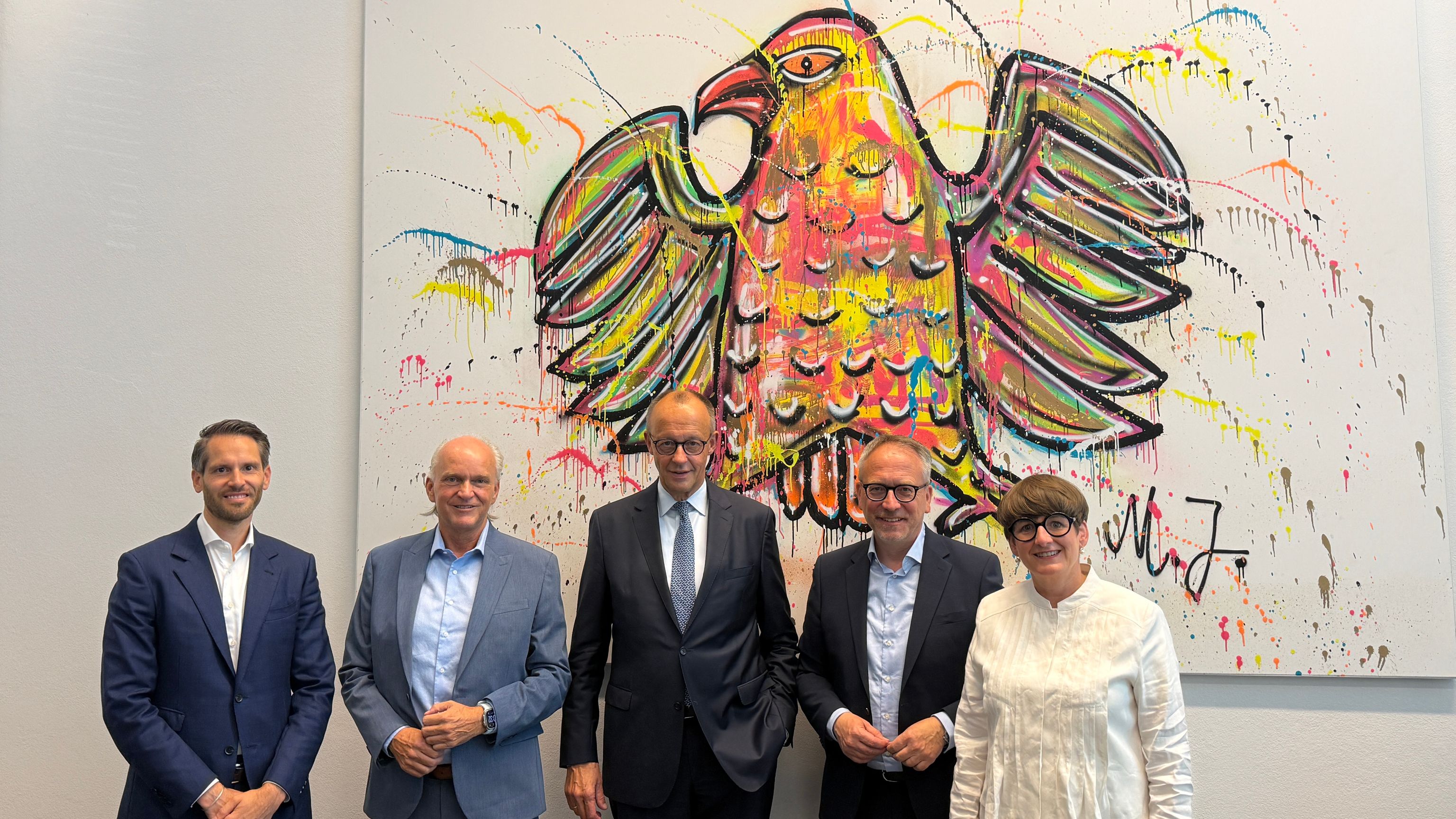 Fünf Personen vor großem, buntem Kunstwerk mit Adler-Motiv.