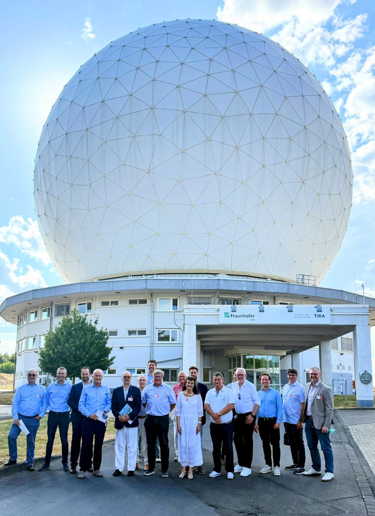 Gruppe vor großem Radom-Gebäude mit metallischer Kuppel, strahlender Sonnentag.