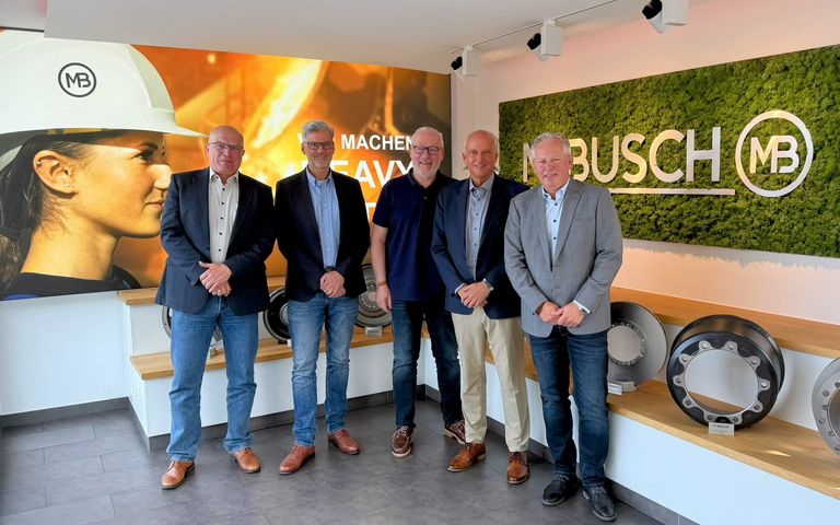 Vier Männer vor Busch-Maschinenhintergrund mit Logo, lächelnd im Gruppenfoto.